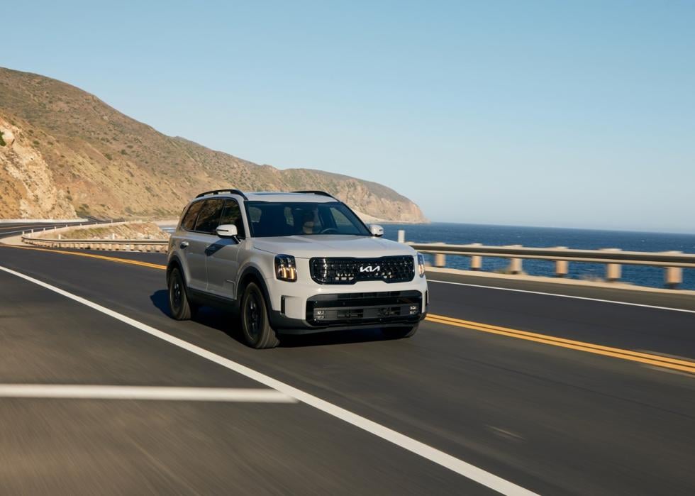 Photo of light-colored Kia Telluride driving near the beach on road.