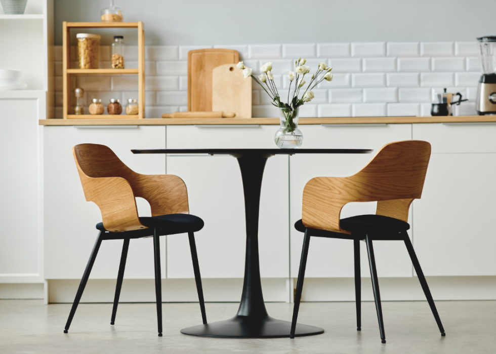 Modern chairs sit around a round dining table in a white minimalist kitchen.