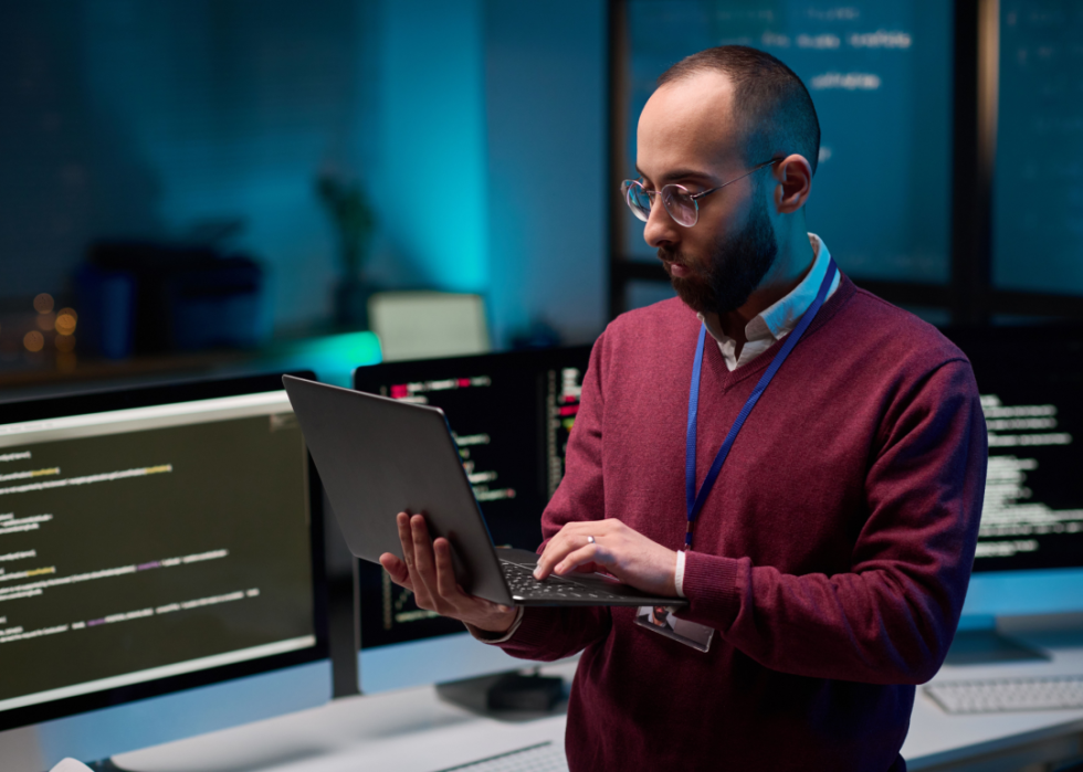 IT technician stands in computer room looking at laptop.