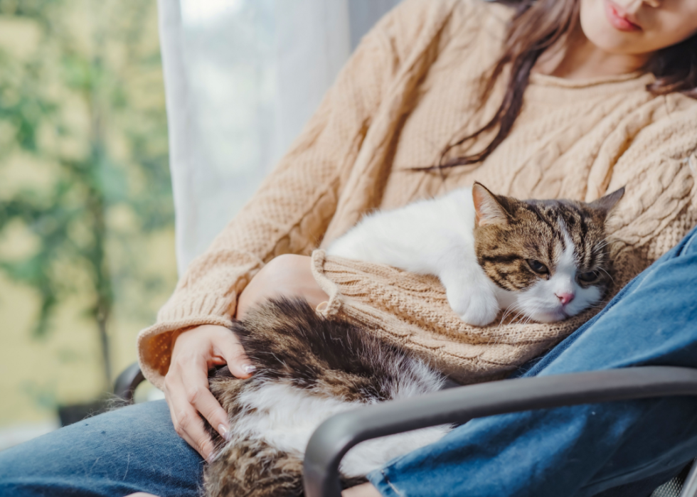 Woman relaxes in chair with cat in arms.