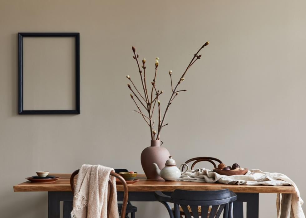 A minimalist kitchen table in an earth-tone room has clay vase with branches arranged.