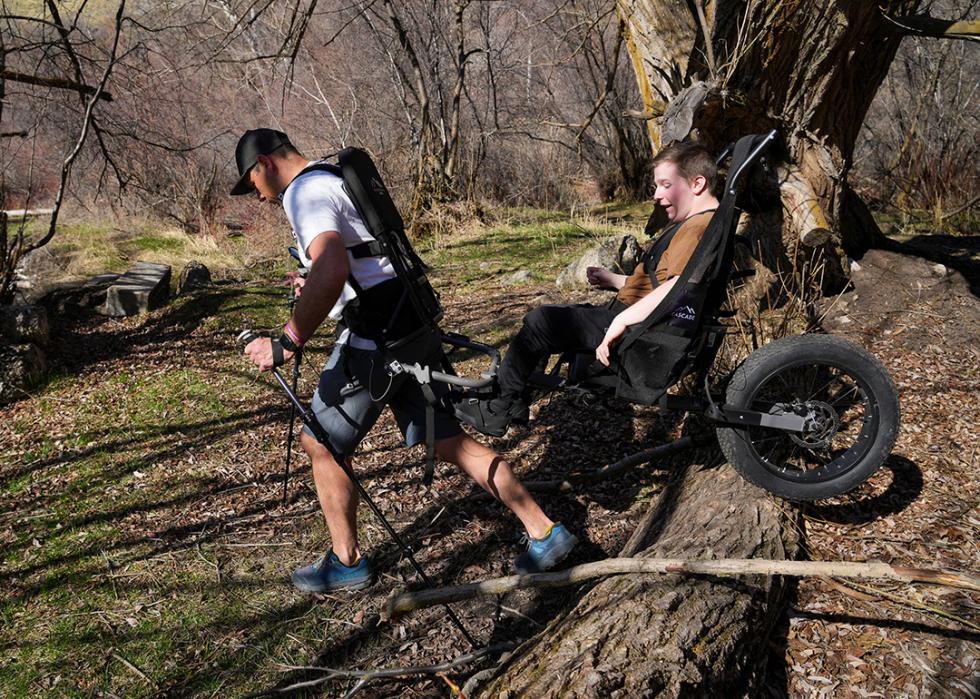 LJ Wilde, the owner of Huckleberry Hiking, pulls Phippin Tingey over a downed log outside Logan with a hiking cart that Wilde designed.