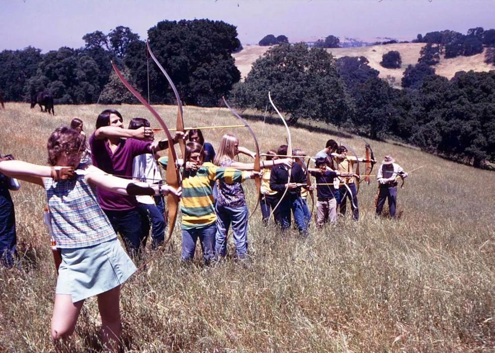 A line of about a dozen kids all aiming with their archery bows