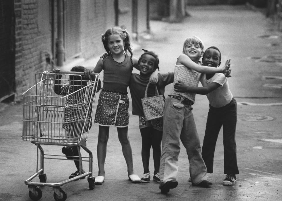 A group of kids with their arms around each other, standing with a shopping trolley on a street in downtown Mount Clemens, Michigan