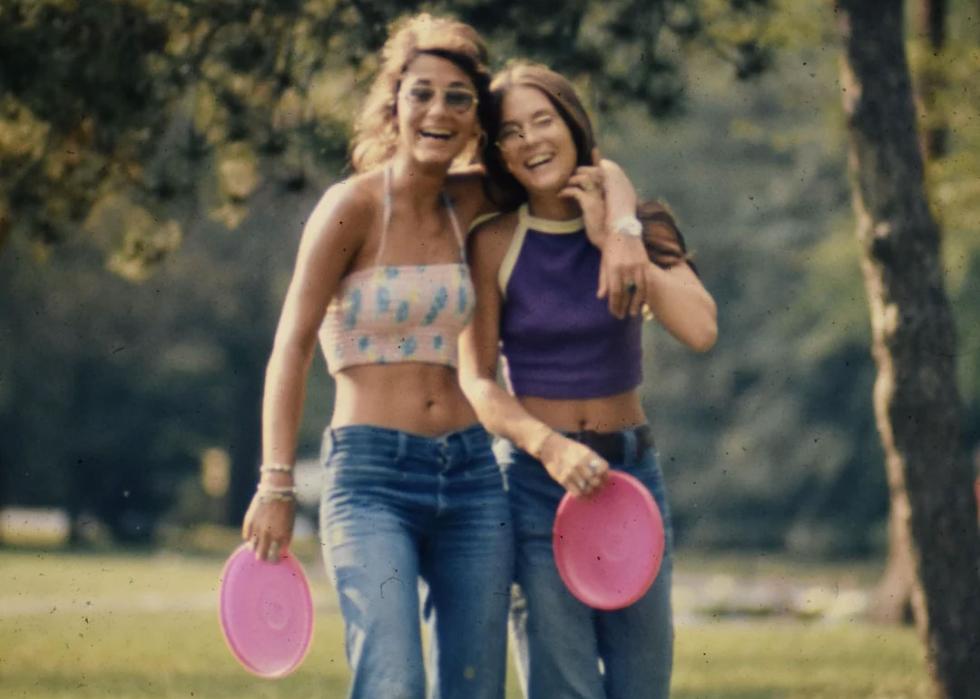 Two young woman holding pink frisbess, laughing