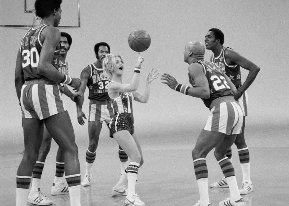 Black and white photo of Goldie Hawn spinning a basketball on her finger, surrounded by the Harlem Globetrotters