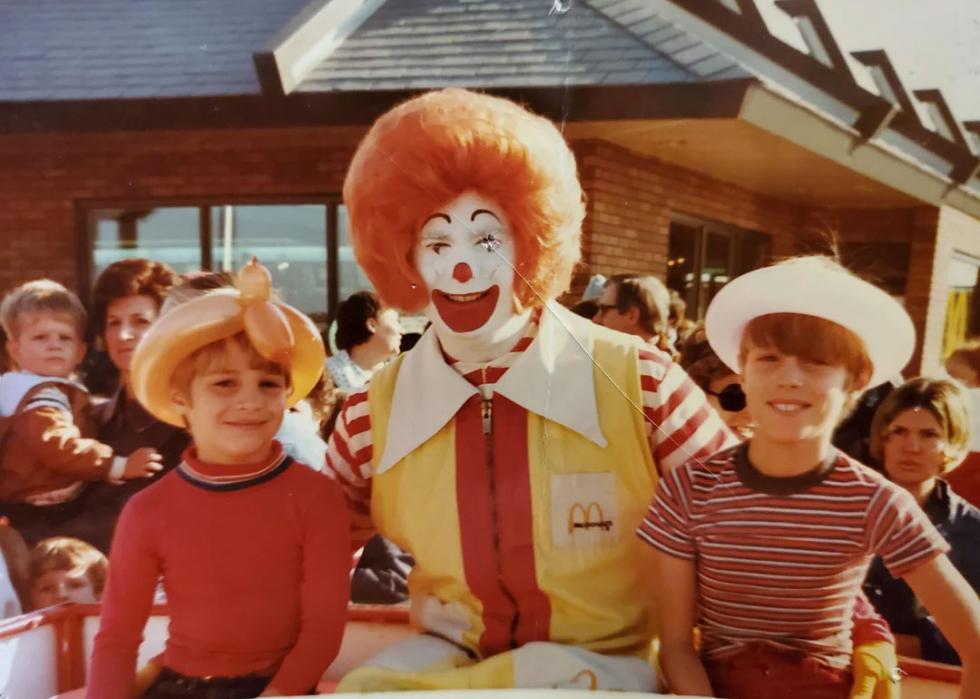 Two boys sitting on either side of a man dressed as Ronald McDonald
