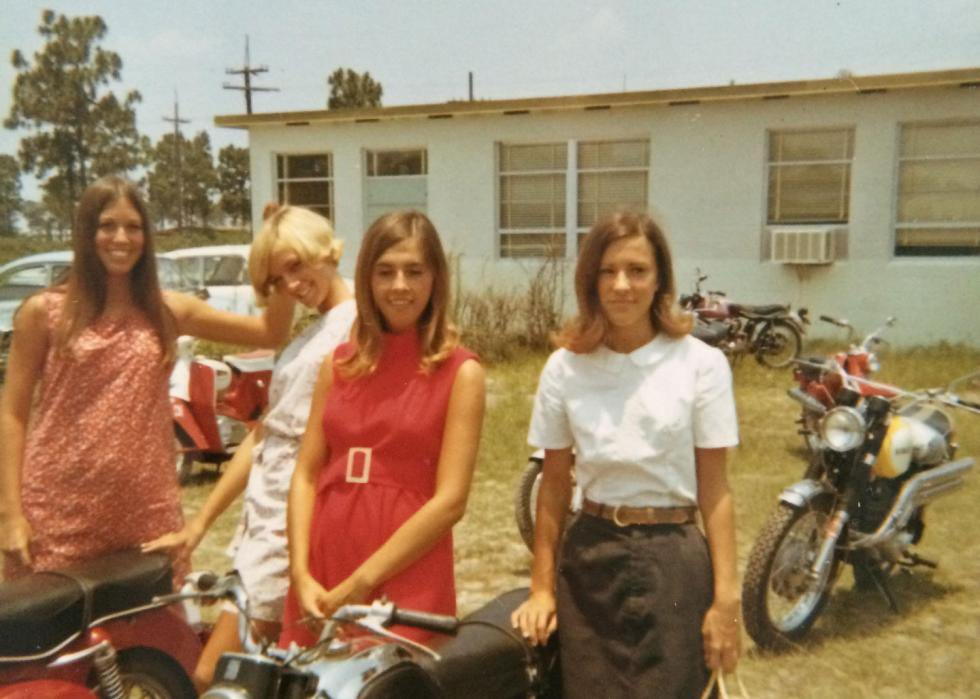 A group of young woman smiling and standing around their motorcycles