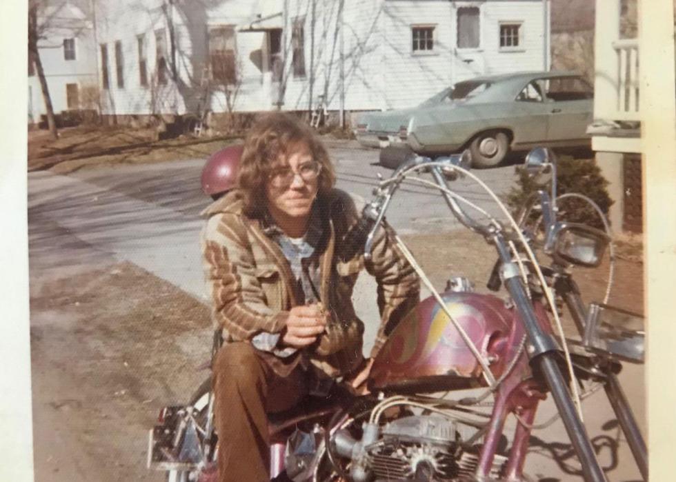 A young man sits on a pink motorcycle in a driveway