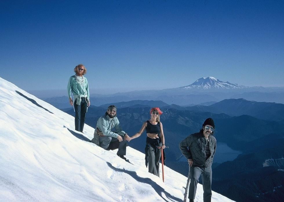 Four people standing on a snowy mountainside with mountain in the distance