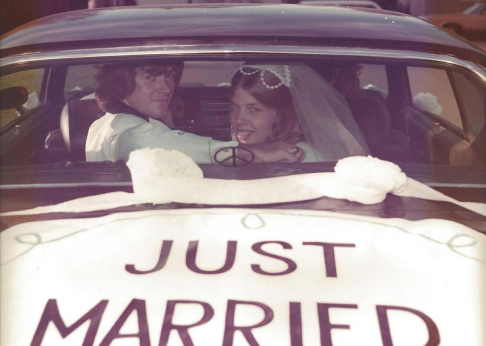 A couple inside a car looking through the back window at the camera. Just Married is painted on the trunk.