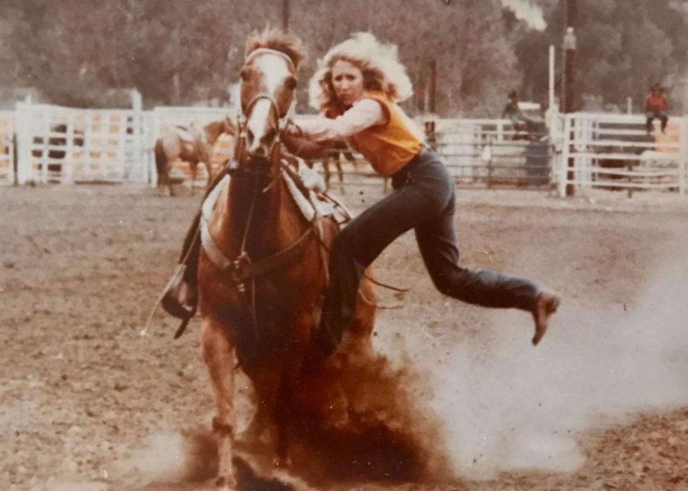 A woman riding a horse in a rodeo, kicking up dust