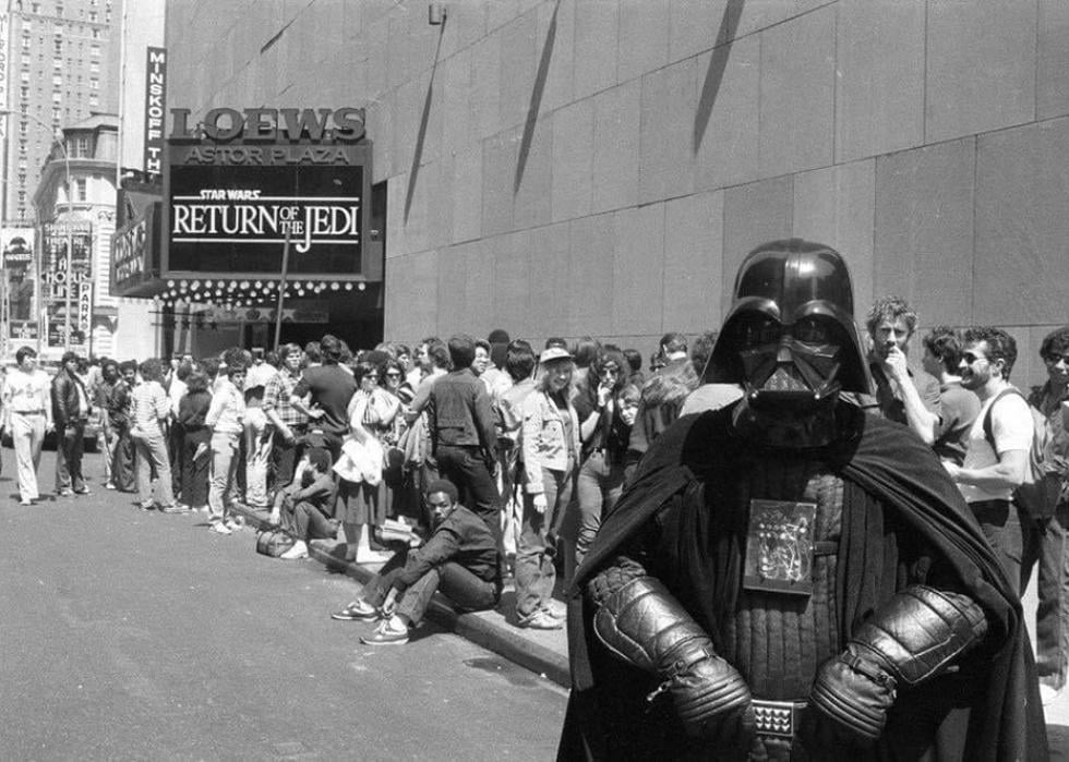 Man dressed up as Darth Vader in front of a long line of people waiting to see Return of the Jedi