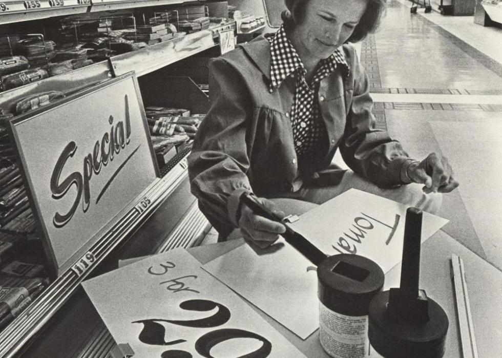 Woman sitting at a table in a grocery store painting the sale signs