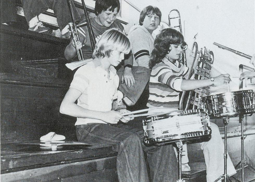 Black and white photo of kids playing music on the bleachers in a gym