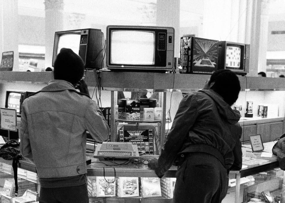 Black and white photo of two teenagers playing Atari at a department store