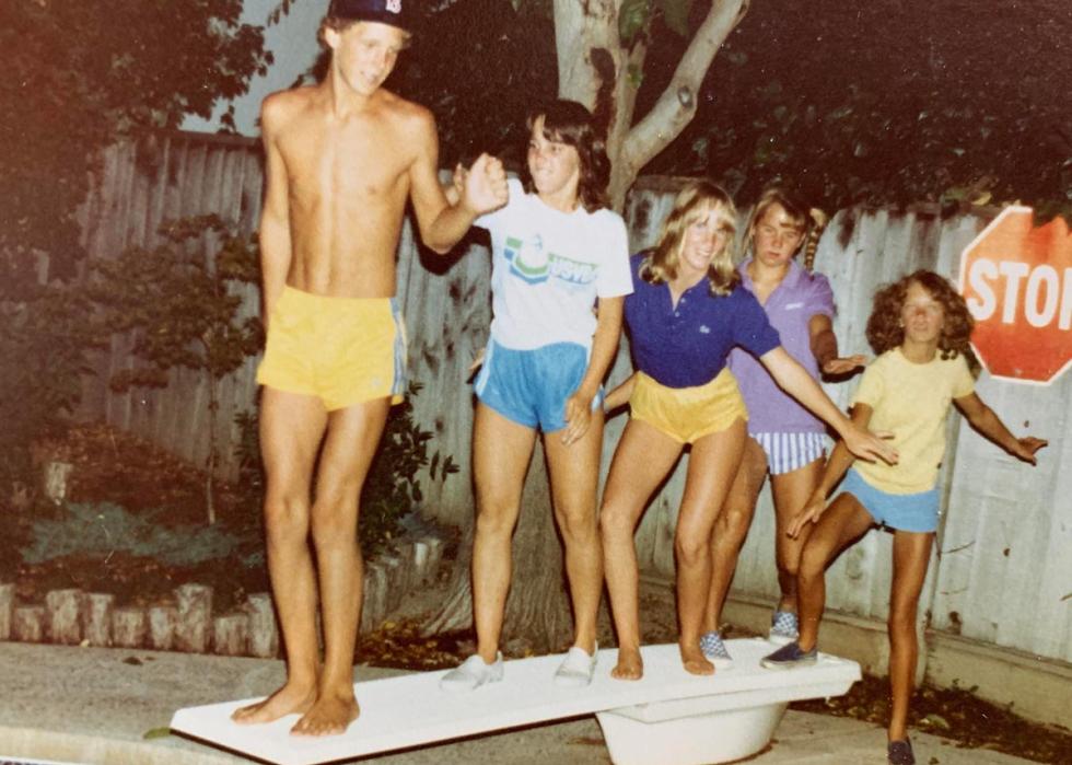 5 teens pose for a photo on a diving board next to a pool