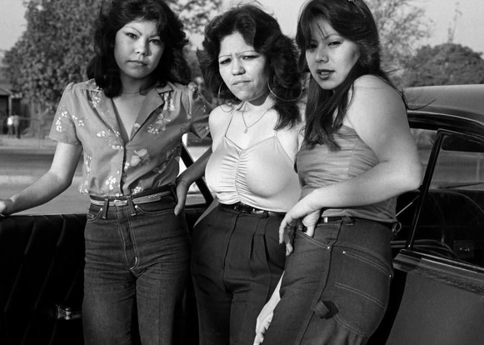 Three women pose for a photo next to a car