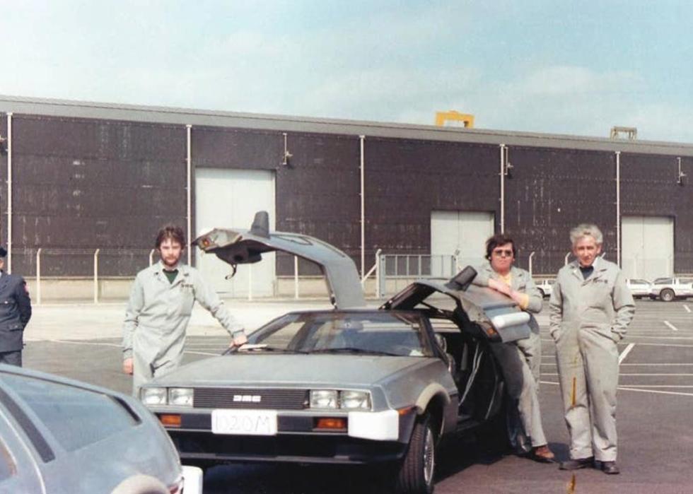 Three men in coveralls pose next to a DeLorean