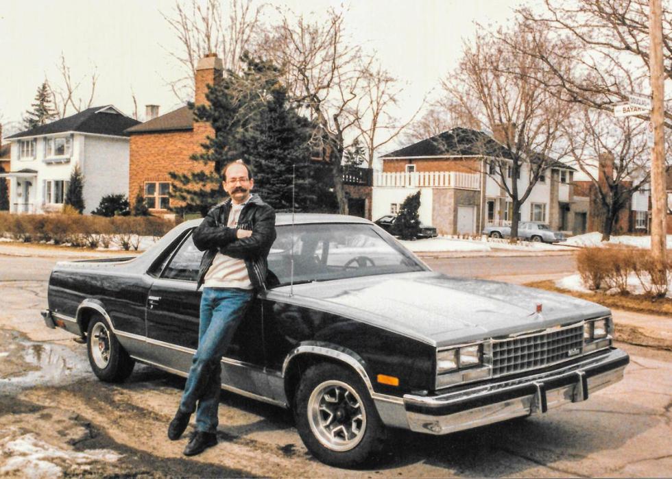 Photo of a mustached man leaning against an El Camino