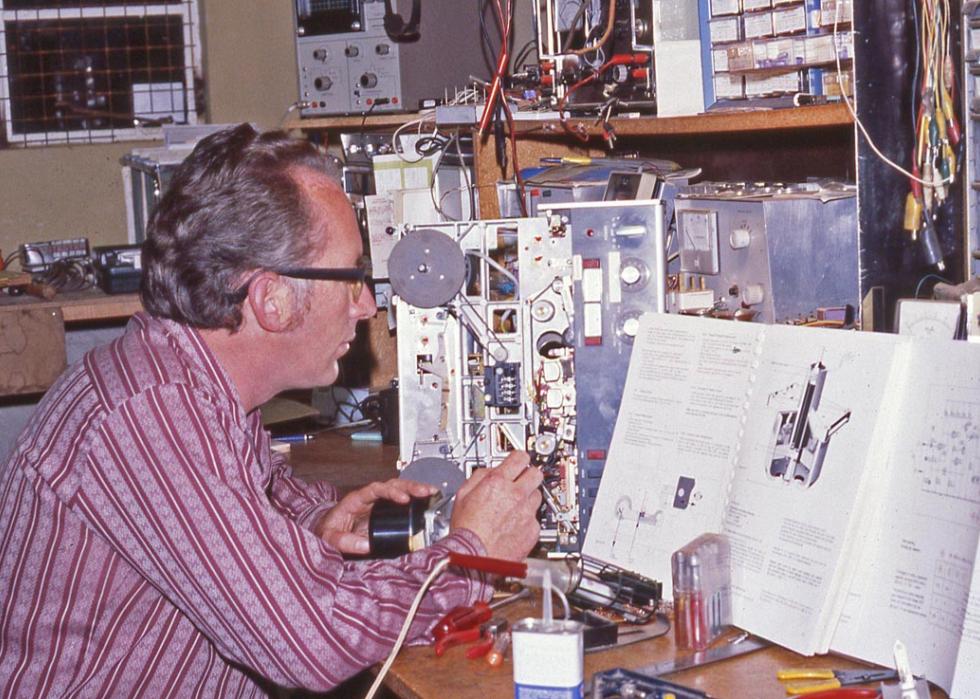 A man looking at an owners manual while trying to repair an electronic device