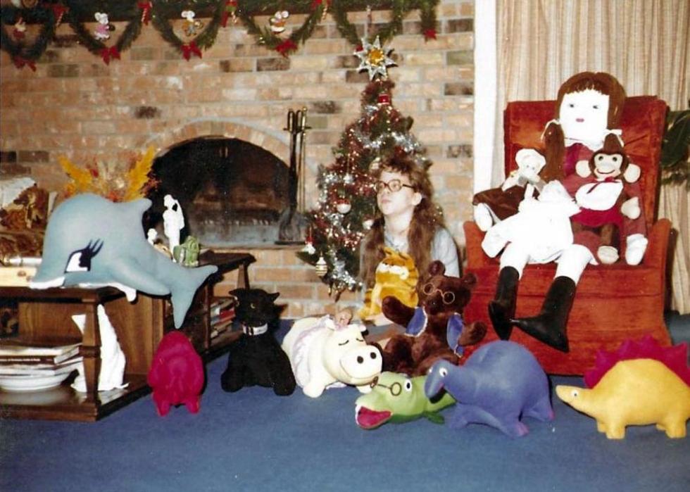 A girl sitting on the floor surrounded by stuffed animals