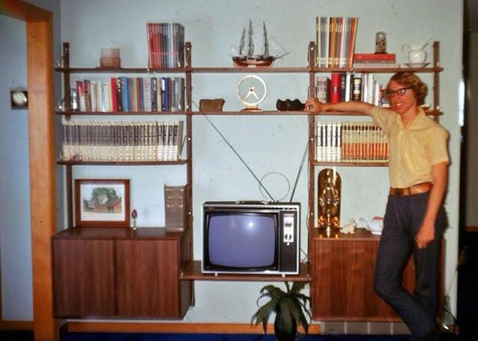 A young man standing in his livingroom next to a very small television