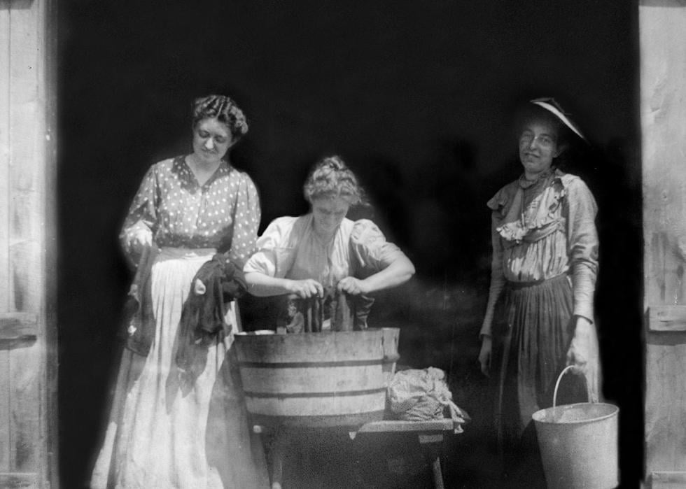 Three women in 1915 washing clothing in front of a barn