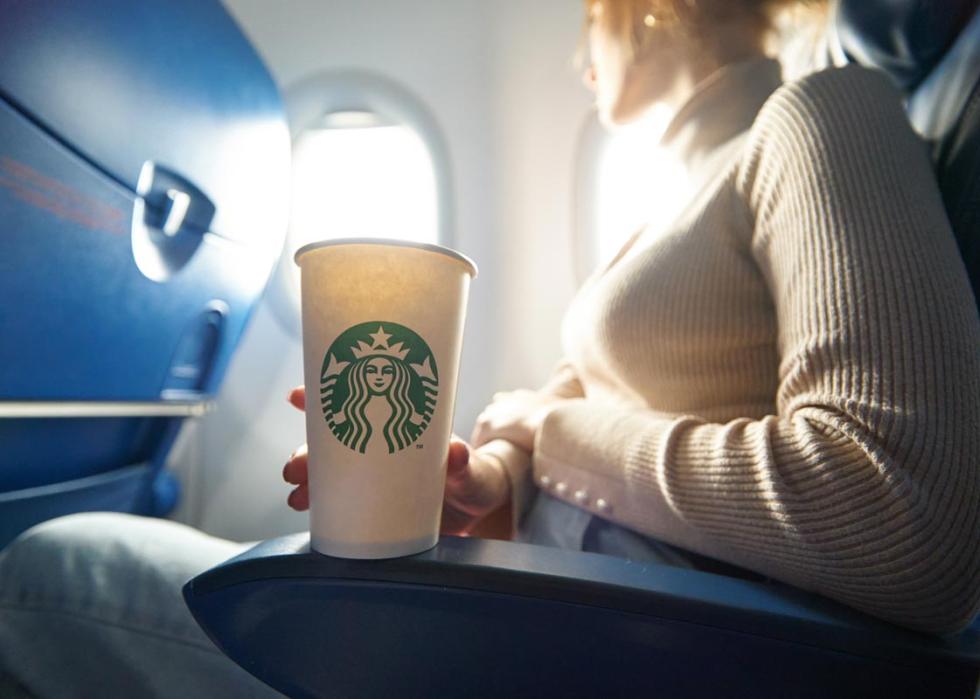 A woman on an airplane holding a Starbucks cup.