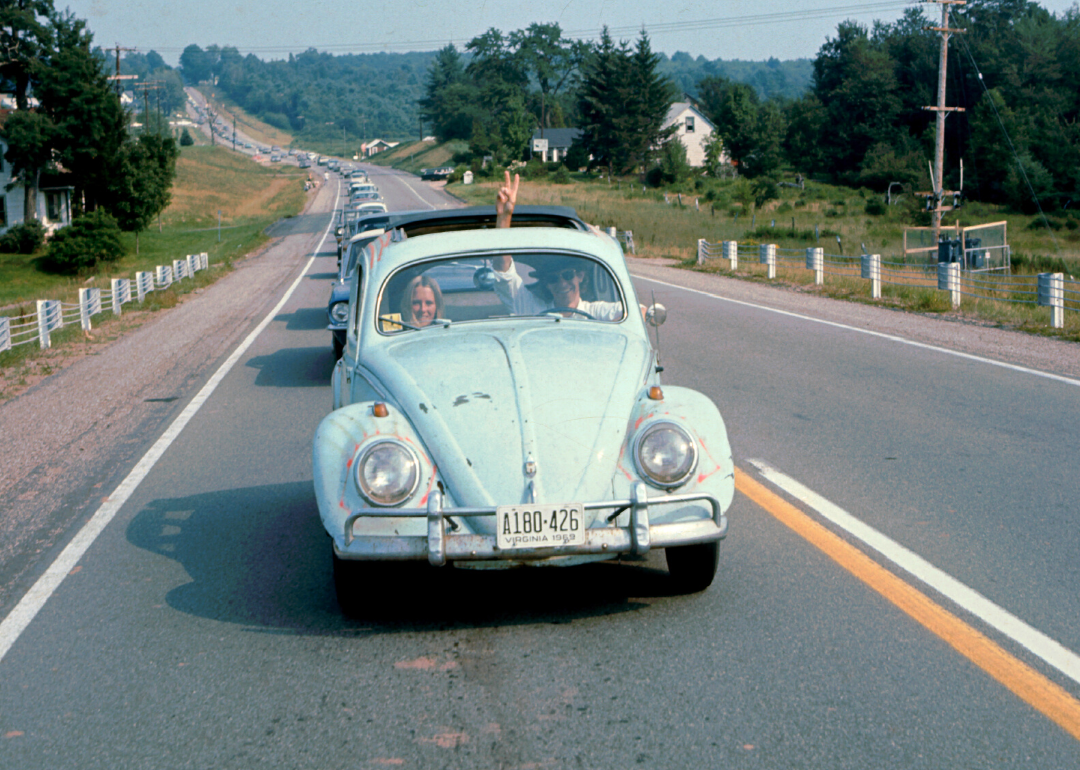 A man driving a volkswagen flashes a peace sign through the sun roof.