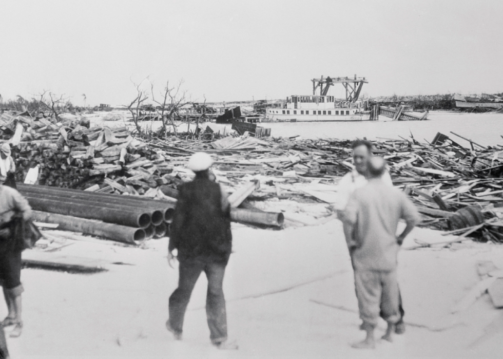 People walking among wreckage along a body of water.