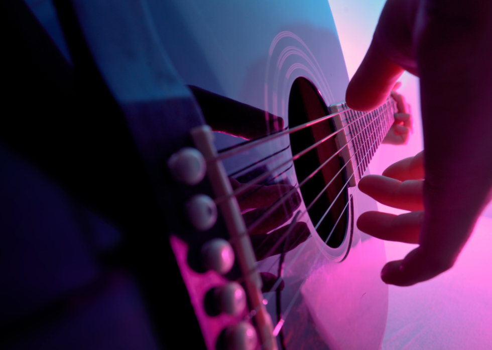 Close-up hand on guitar with pink and purple lights.