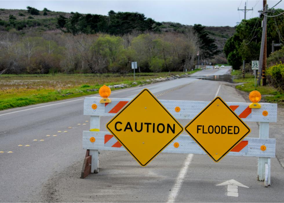 Photo shows a medium shot of a road blocker with signs that read "Caution" and "Flooded"