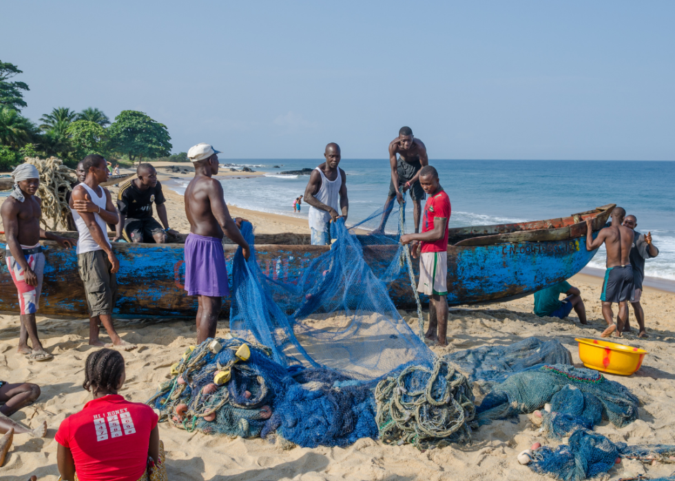 Fishermen sorting nets on wooden boat at beach in Robertsport
