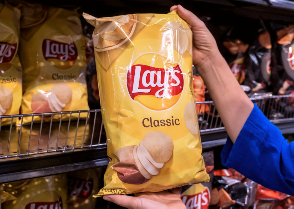 Hand holding a bag of Lay's Chips in supermarket.