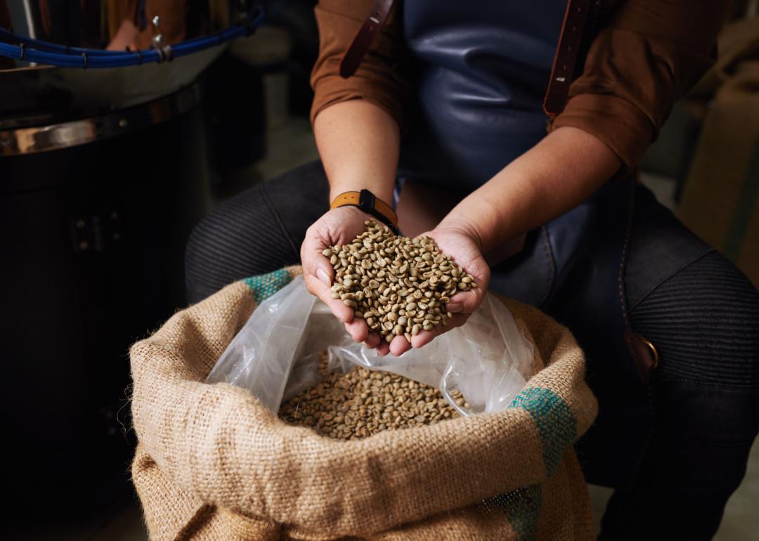 Person holding green coffee beans over burlap bag.