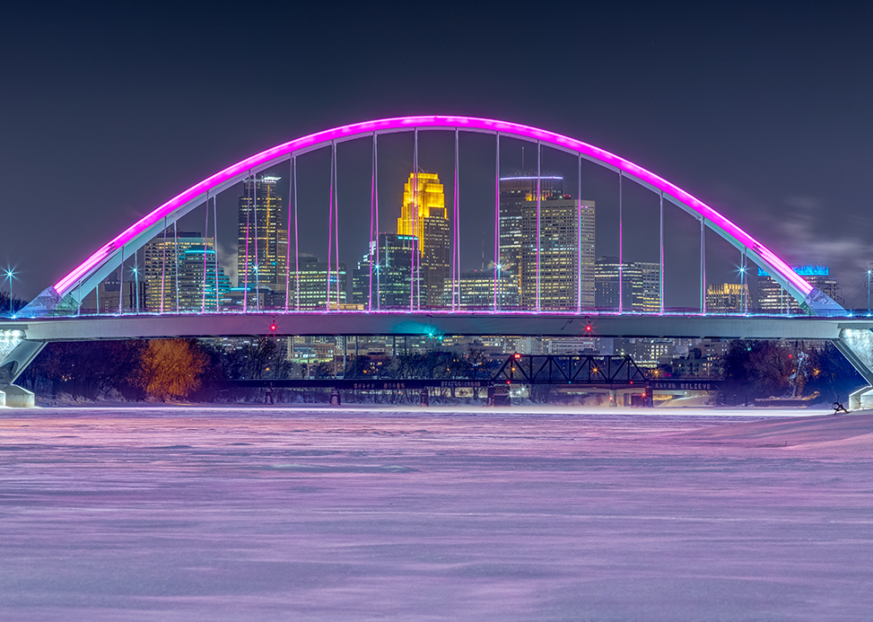 A frozen, snowy Mississippi River and magenta colored Lowry Bridge with Minneapolis skyline.
