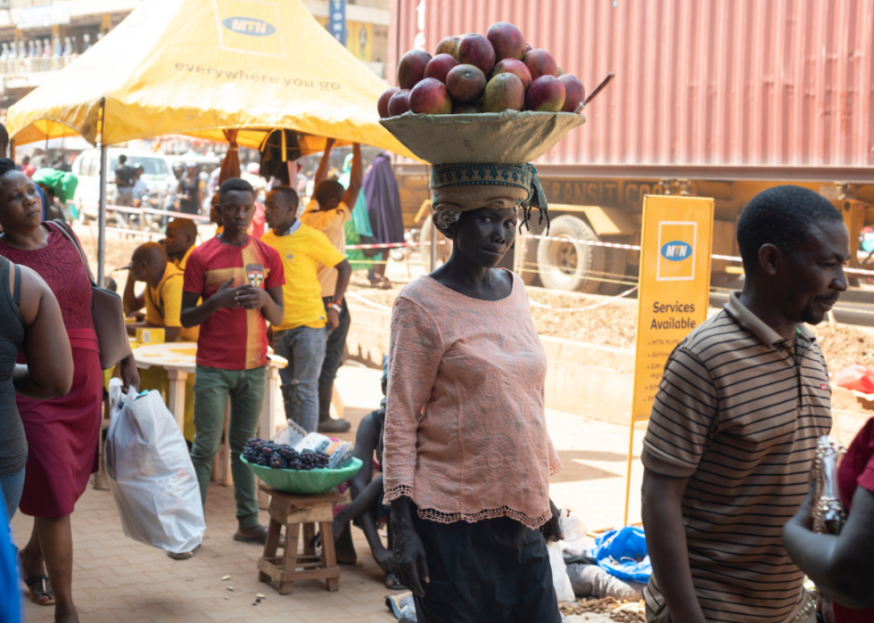 Woman walking on busy street in Kampala with basket of mangos