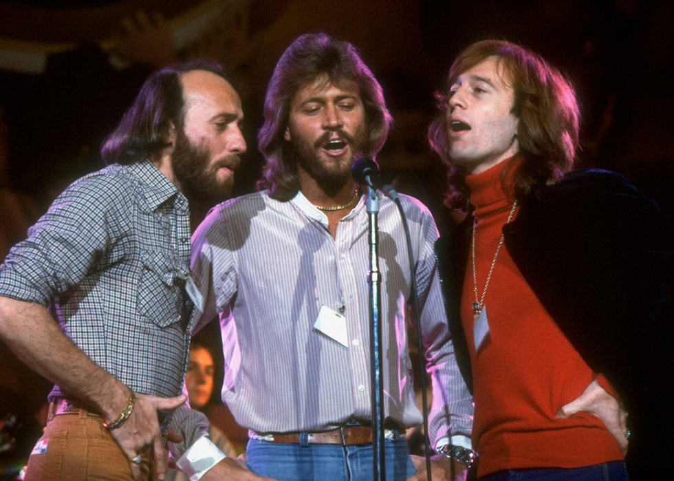 Maurice, Barry, and Robin Gibb of the Bee Gees singing on stage.