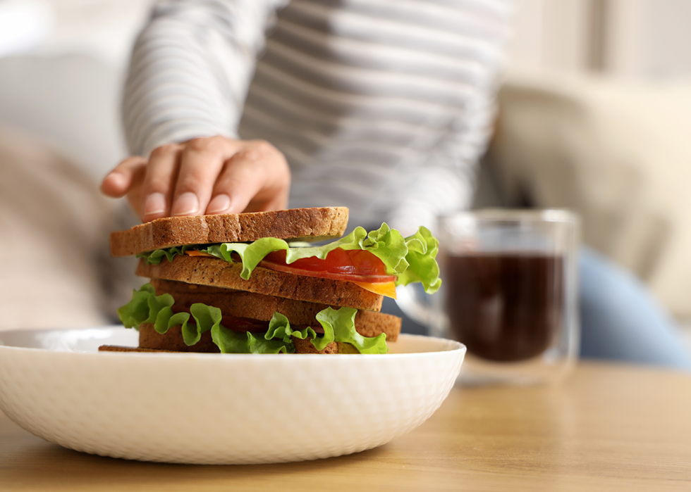 Hand reaching for a sandwich on table.