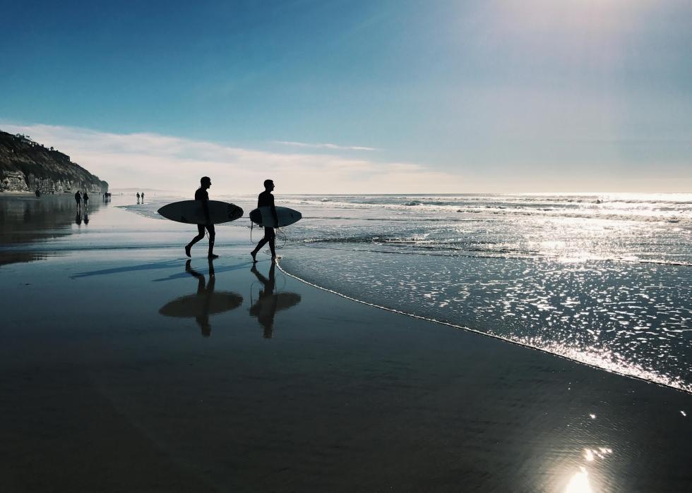 People walking with surfboards on beach.