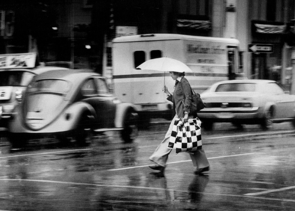 A person carrying an open umbrella across a city street.