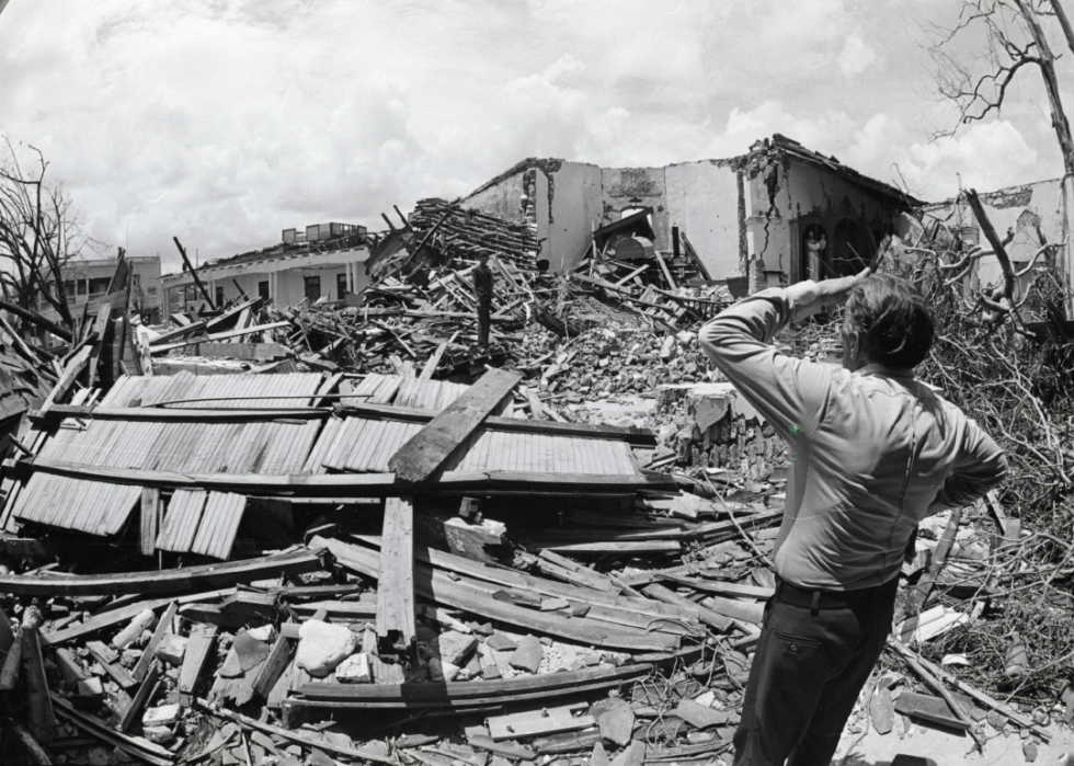 A person looks over a destroyed house surrounded by wreckage.