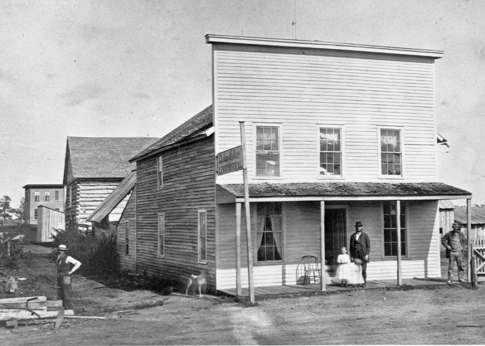 Two story wooden building with porch and people in rural town.