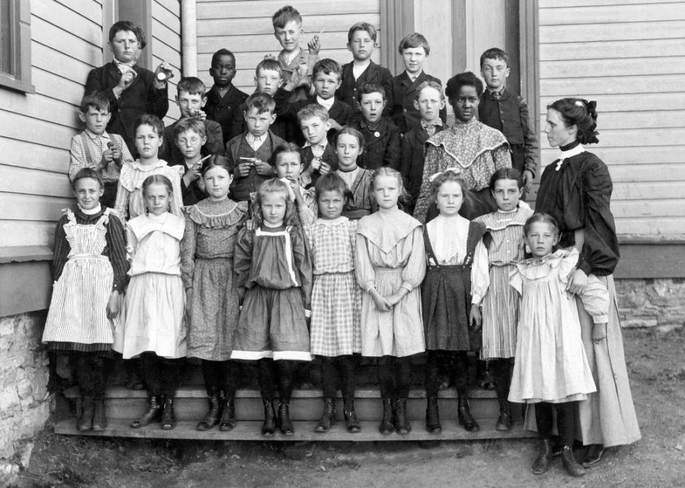 Group of children pose with their teacher outside schoolhouse