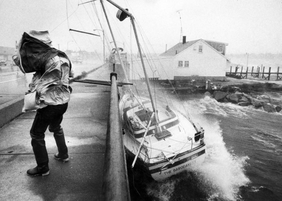 Waves pushing a boat against a wall while a person on the pavement trying to cover their head from the storm.