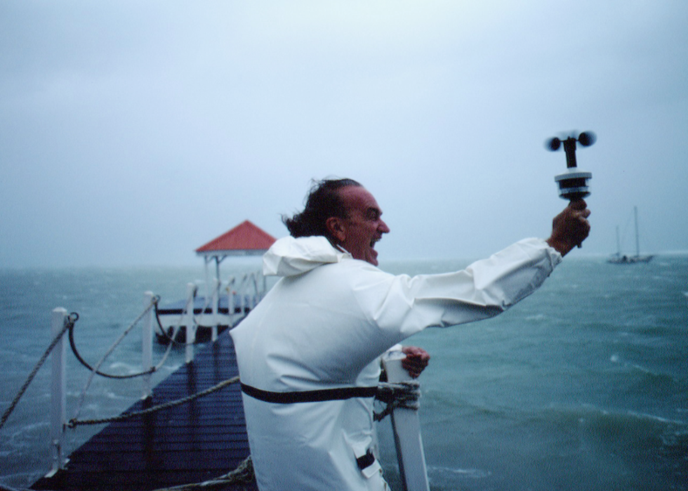 A man holding a wind measuring device on a dock in extreme wind.