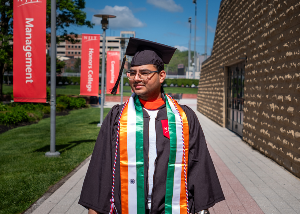Graduate standing on the campus of NJIT in cap and gown.
