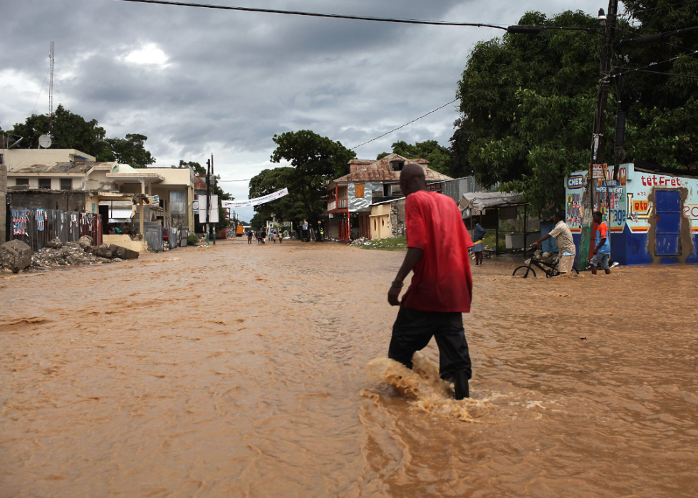 A man treads through ankle-deep muddy water on a flooded street with a handful of businesses.