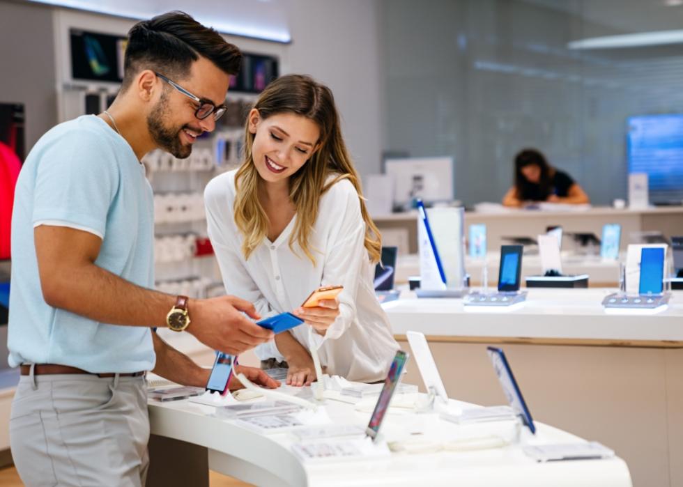 A young man and woman are holding smartphone devices in their hands in tech showroom.